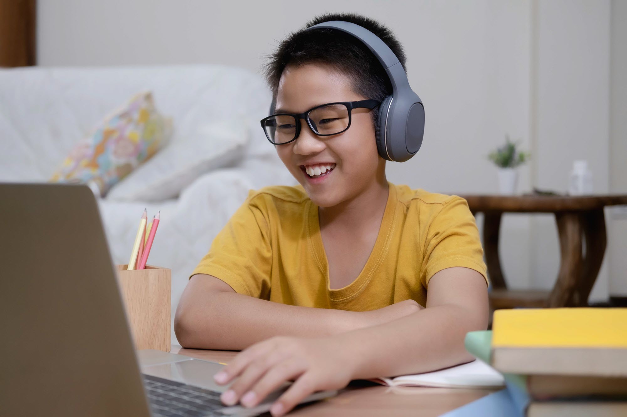 Boy with headphones on, sitting at home desk, smiling at laptop screen